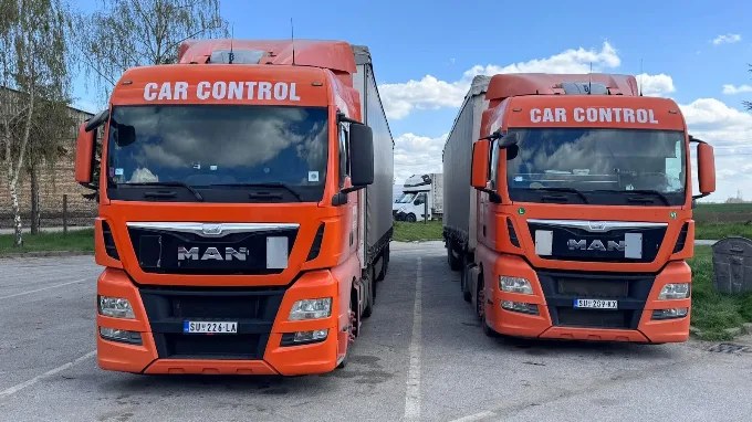 Dva narandžasta MAN TGX kamiona sa natpisom Car Control i ceradnim prikolicama